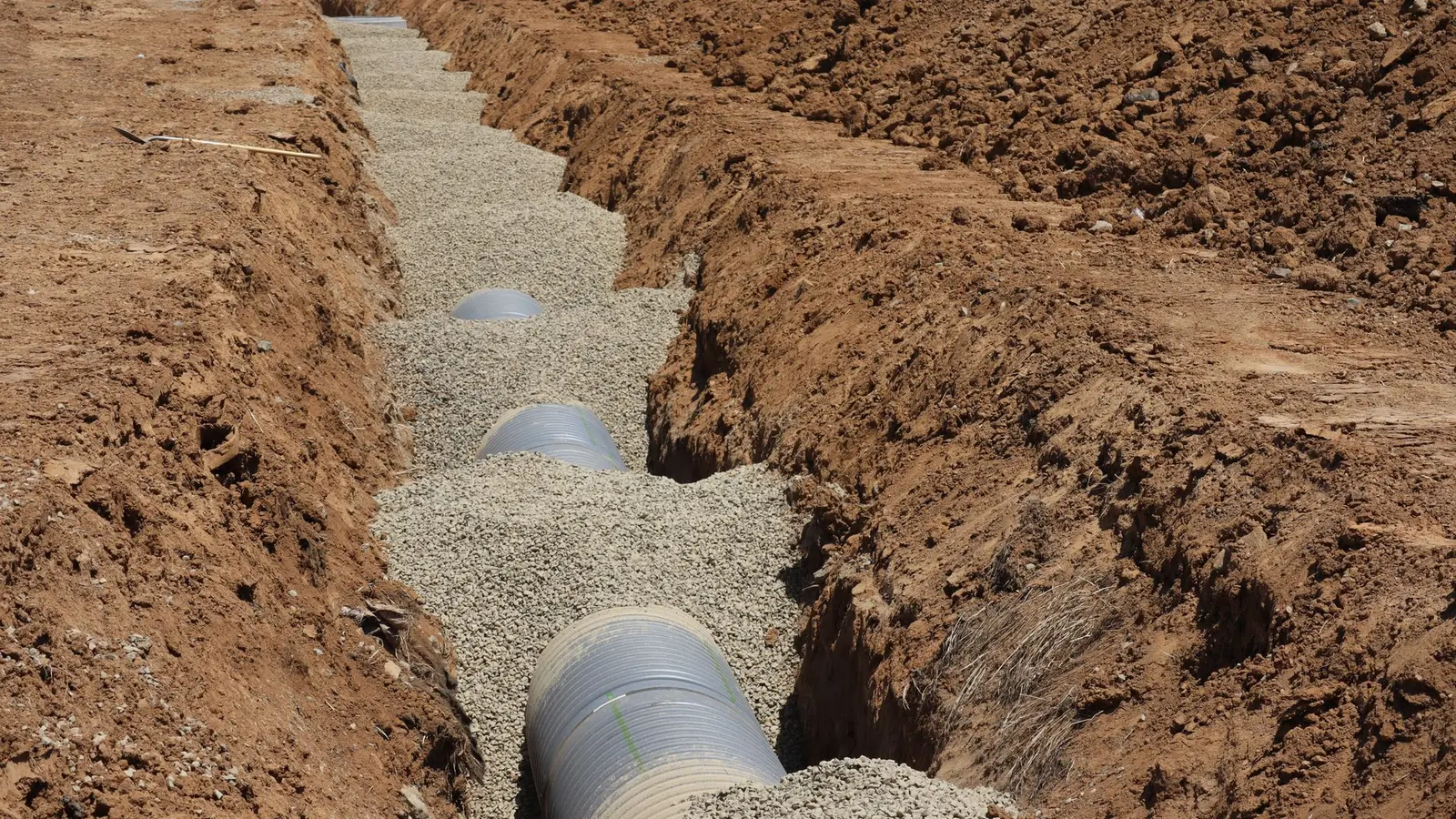 Perforated drain pipe laid on gravel in a freshly dug trench