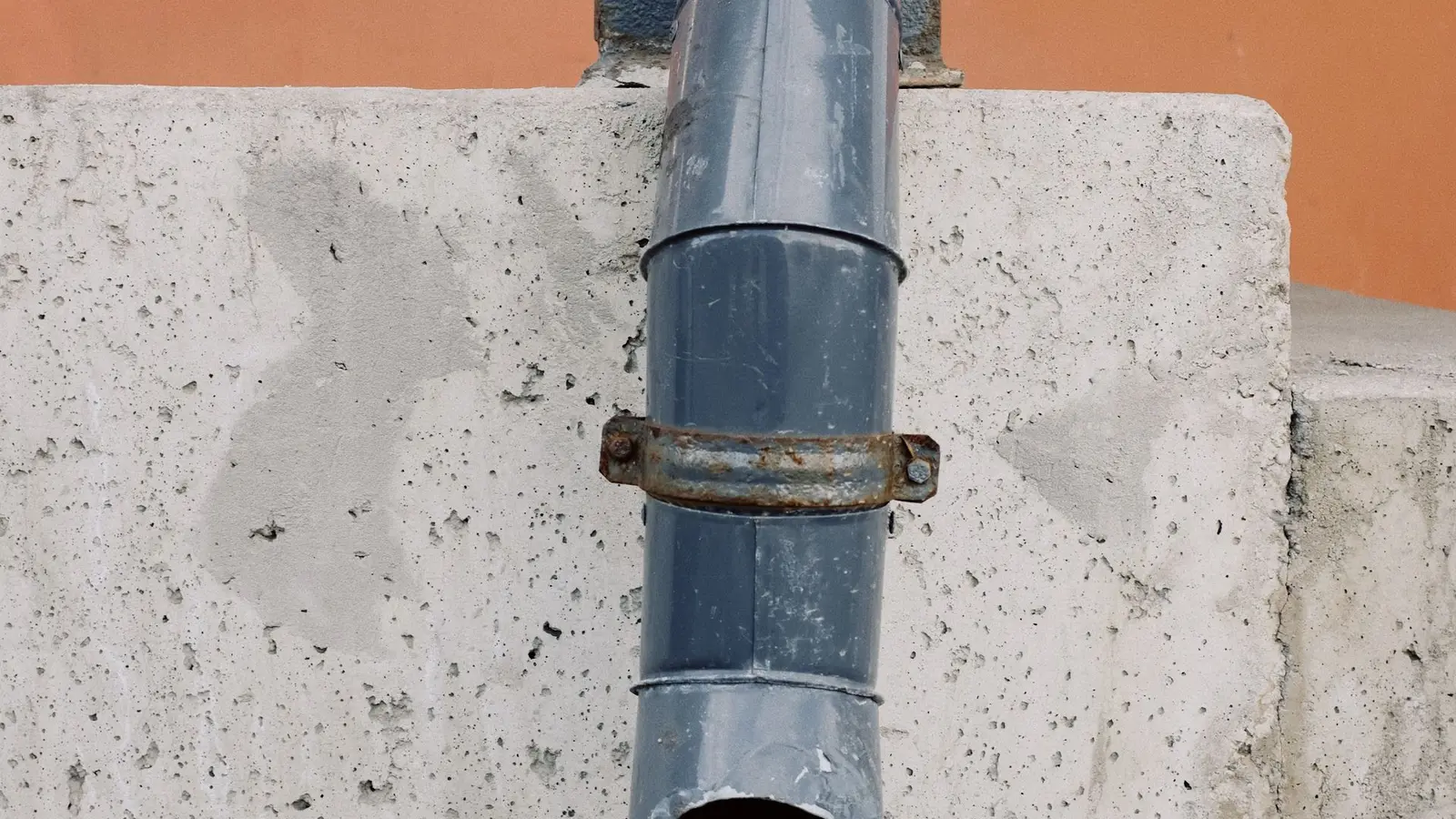 Metal downspout ending above wet paving stones beside a concrete ledge